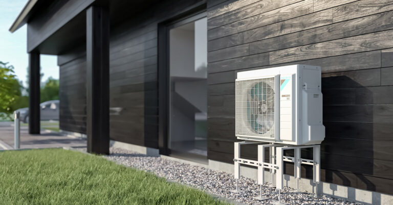 Ilma-vesilämpöpumpun ulkoyksikkö mustaa talon seinää vasten.